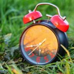 Classic red alarm clock resting on vibrant grass, symbolizing the passage of time.