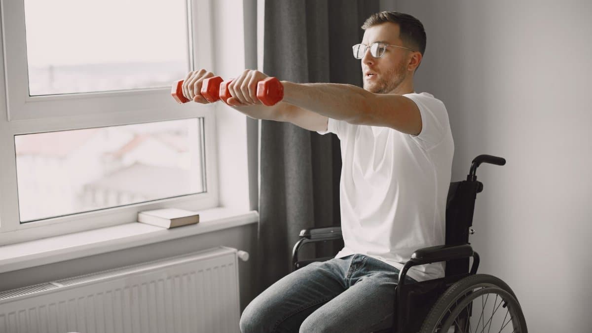 Man in wheelchair working out with dumbbells by window, promoting an active lifestyle.