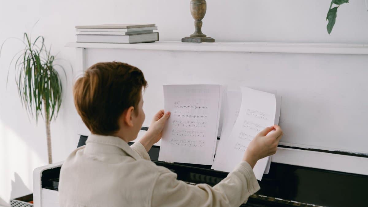 Boy sitting at piano holding music sheets, showcasing learning and skill development indoors.
