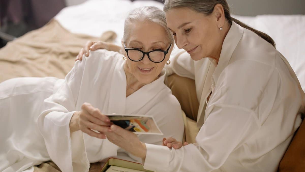 Senior women in bathrobes bonding over cherished photo memories indoors.