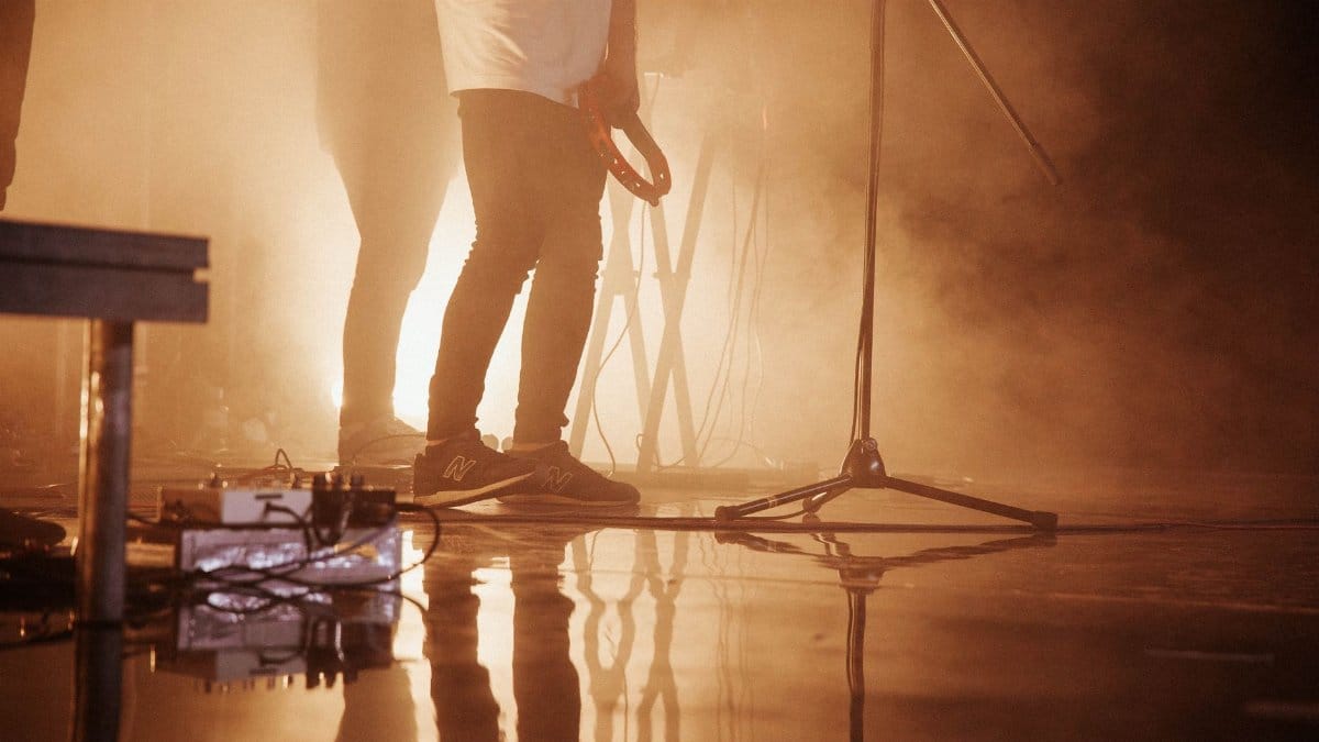 Men performing on a dramatic smokey stage with musical instruments and reflections.
