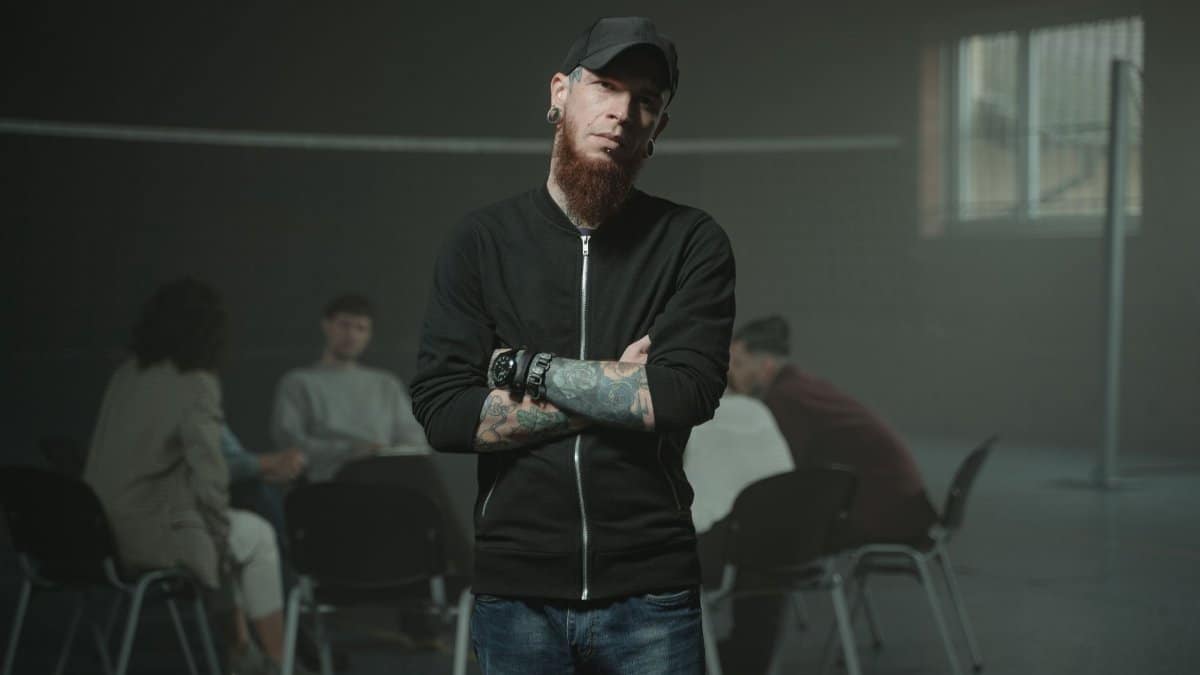 A bearded man stands confidently with arms crossed in a group therapy session.