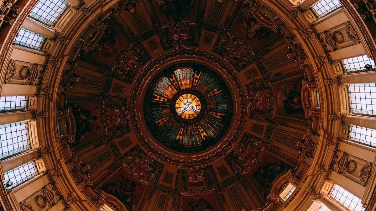 Intricate church dome interior with stunning stained glass and symmetrical design, viewed from below.