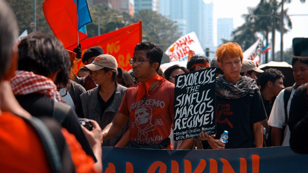 Group of protesters marching with signs and flags in an urban setting, advocating for political change.