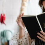 Close-up of a woman reading a menu indoors with a blurred cozy kitchen background.