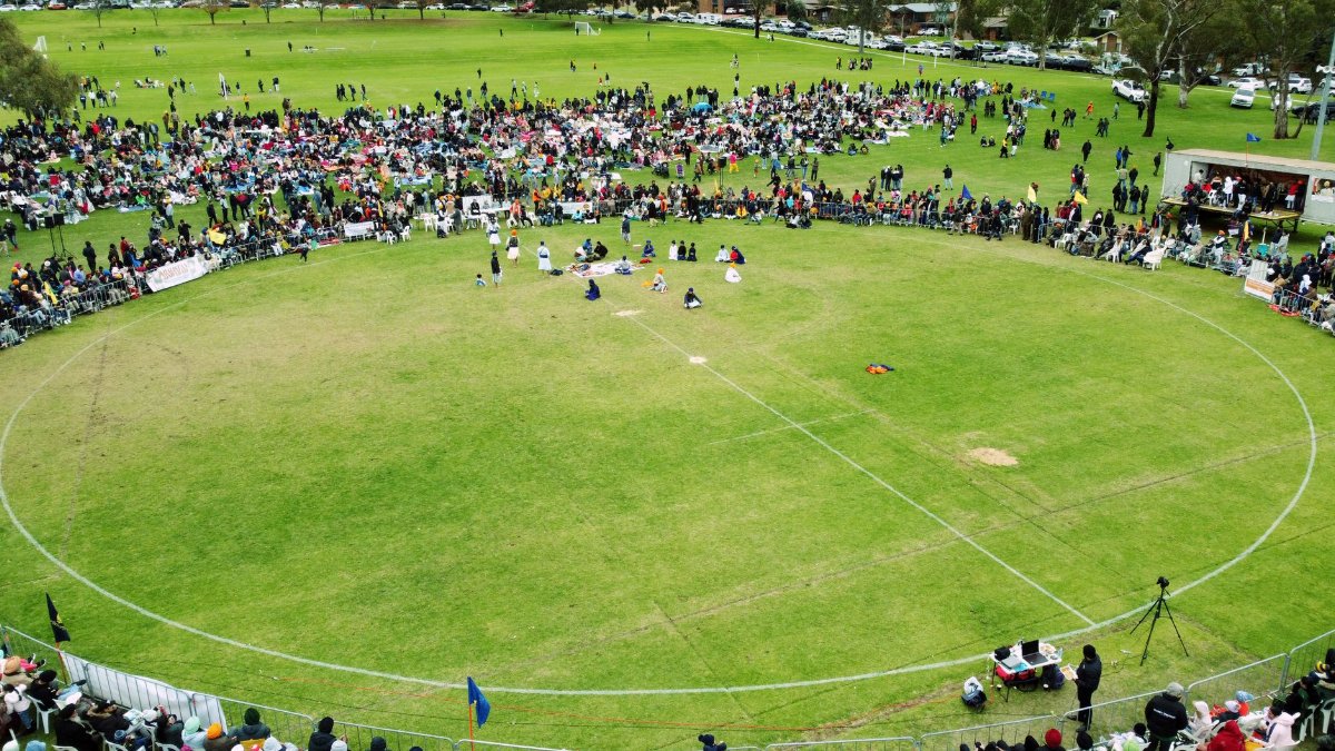 Aerial view of a large crowd gathering in a circular grassy area during the day.