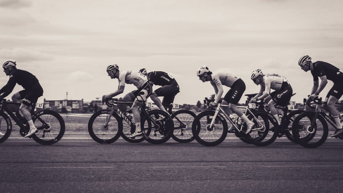 Monochrome photograph of a fast-paced road cycling race with multiple cyclists in action.