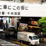 Bustling street view in Tokyo, Japan, with colorful umbrellas and vehicles during a rainy day.