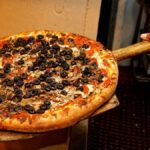 Appetizing pizza with olives and mushrooms being served fresh from the oven.