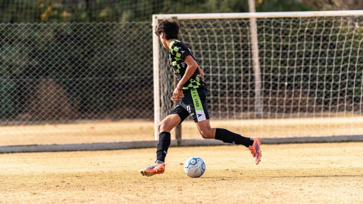 A young male soccer player dribbling a ball during a daytime match on a field.