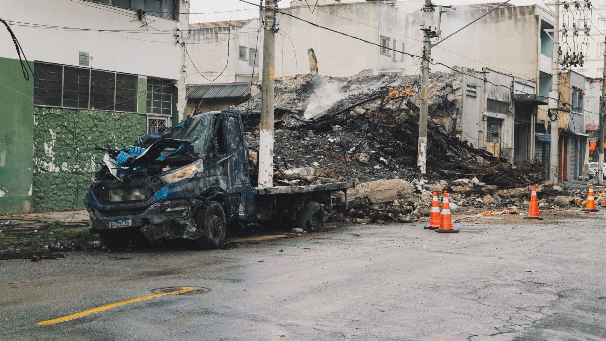 A damaged vehicle and debris on an urban street after a fire incident, depicting aftermath and destruction.