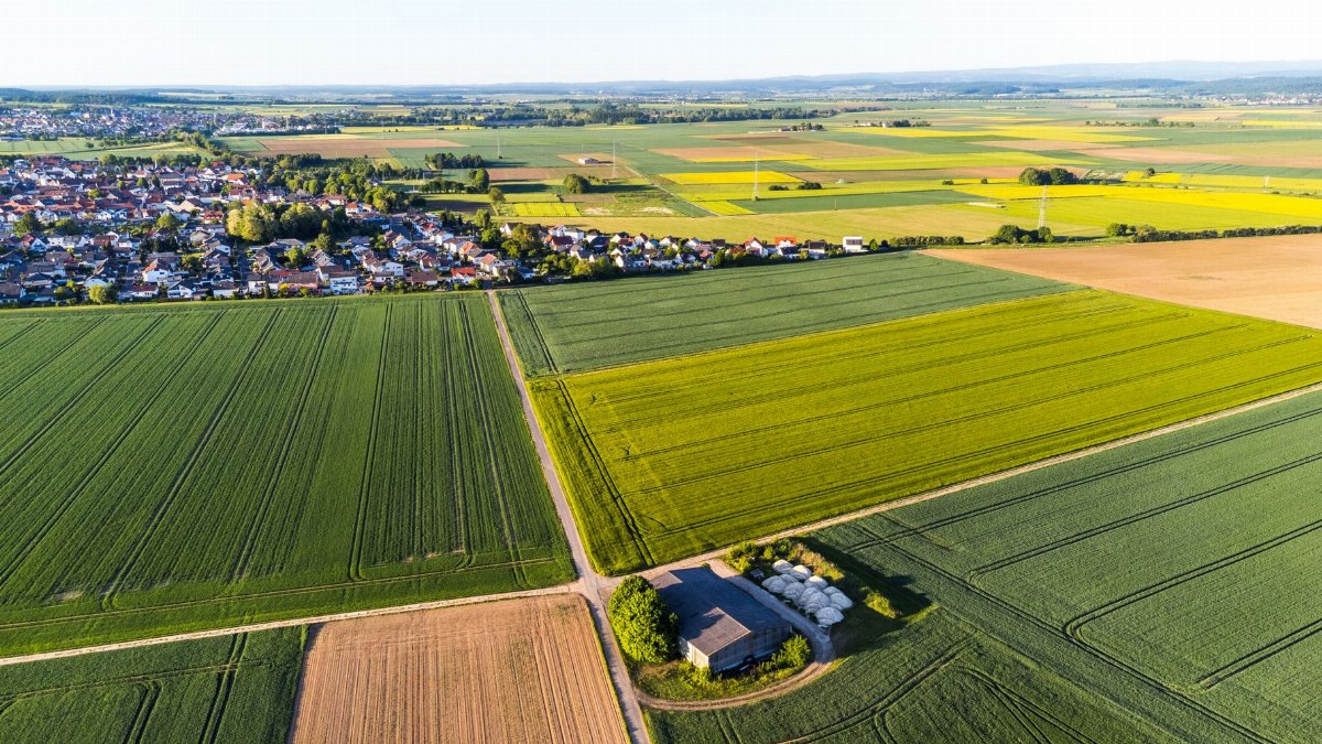 A scenic aerial capture of fields and a nearby village under a clear sky.