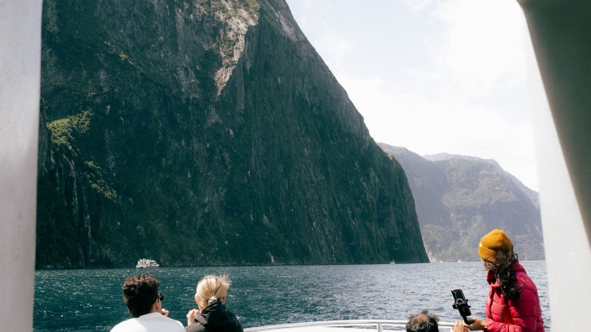 Tourists enjoying a boat tour at Milford Sound, Southland, New Zealand, with stunning mountain views.