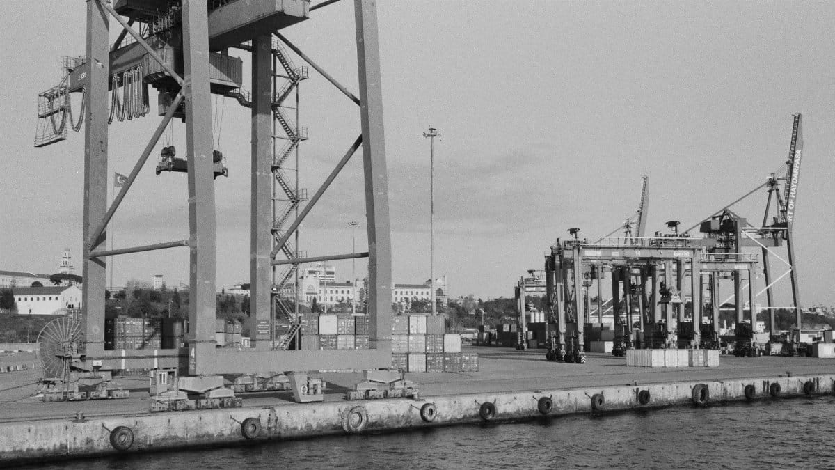 Black and white image of a shipping port featuring massive cargo cranes and containers.