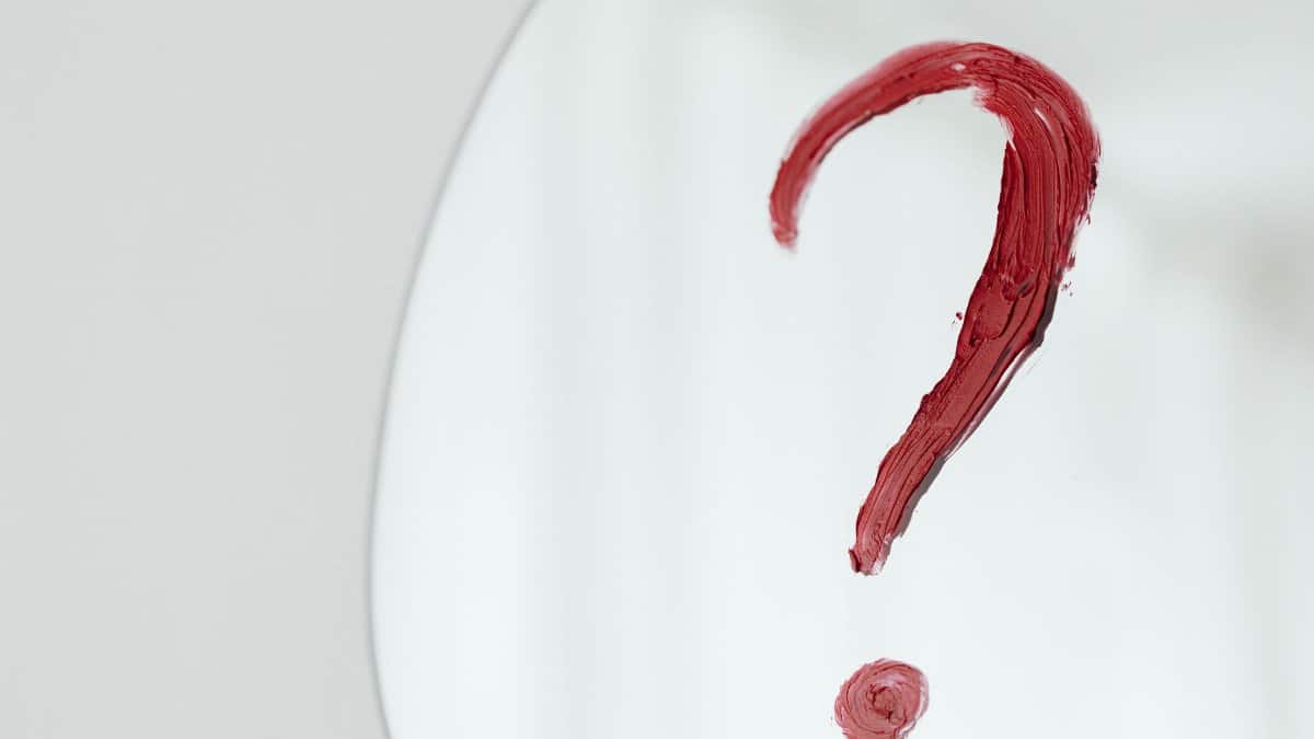 Close-up of a red question mark painted on a mirror with a white background.