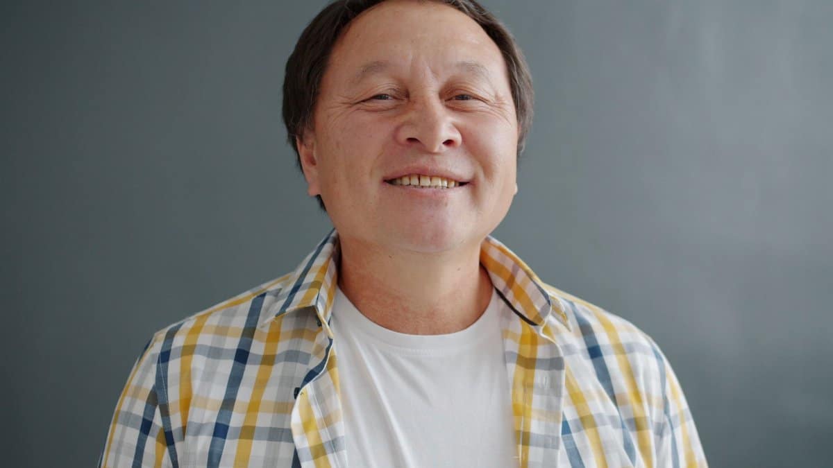 Close-up portrait of a smiling man wearing a plaid shirt, exuding warmth and positivity.