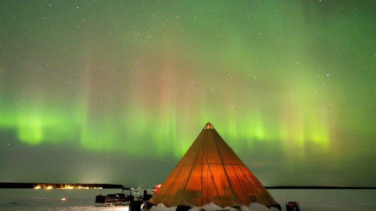 A stunning view of the Northern Lights over a tent in snowy Luleå, Sweden, beautifully captured at night.