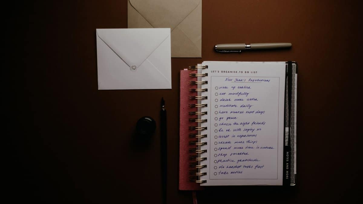 Overhead view of a to-do list notebook with New Year's resolutions, pens, and envelopes on a desk.