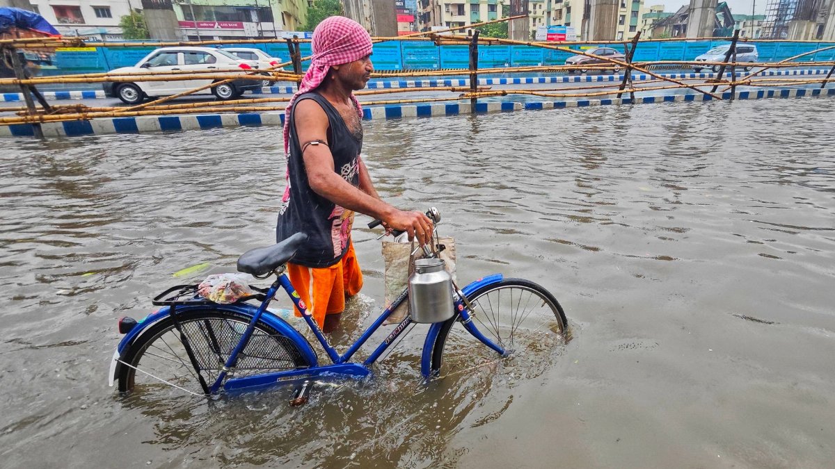 A man pushes a bicycle through flooded city streets in Kolkata, India during a rainstorm.