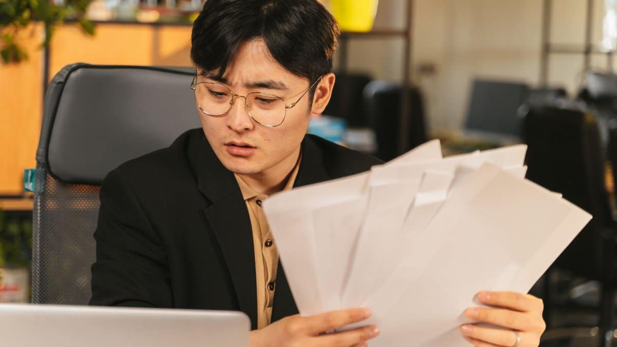 Businessman in glasses reviewing paperwork in a modern office setting.