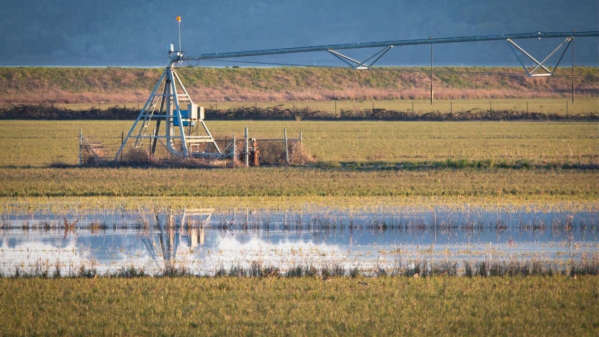 A flooded farm field with an irrigation system and reflection under cloudy skies.