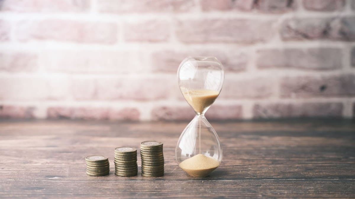 Hourglass and stacked coins on wood, symbolizing the concept of time and money.