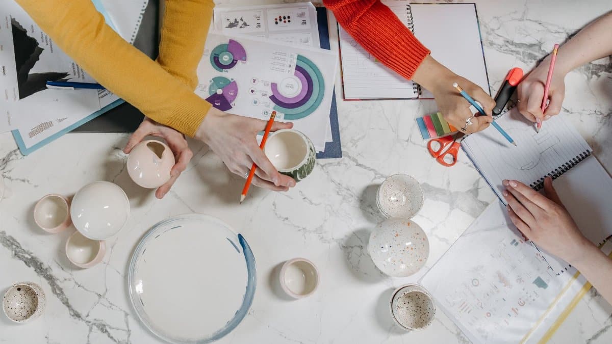 Team working on ceramic projects and charts at office table from top view.