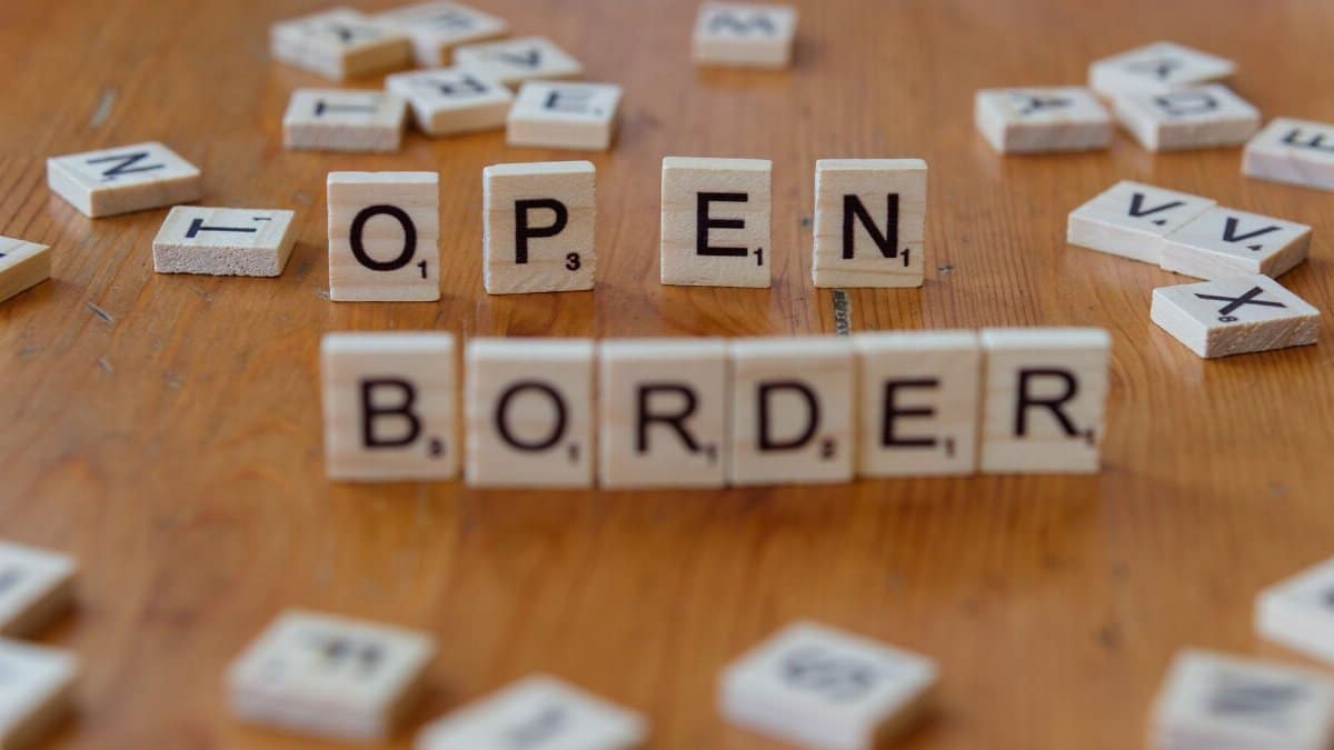 Wooden Scrabble letters on a table spelling out 'open border', concept of migration and geopolitics.