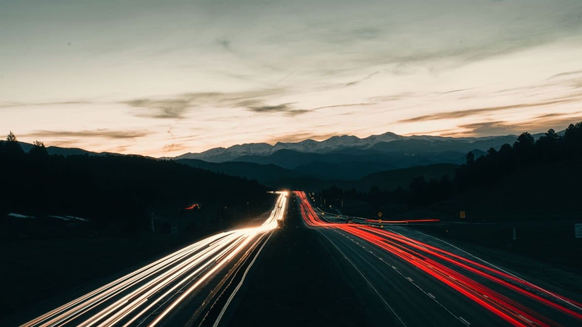 Captivating long exposure of highway light trails under Colorado's twilight sky, featuring distant mountains.