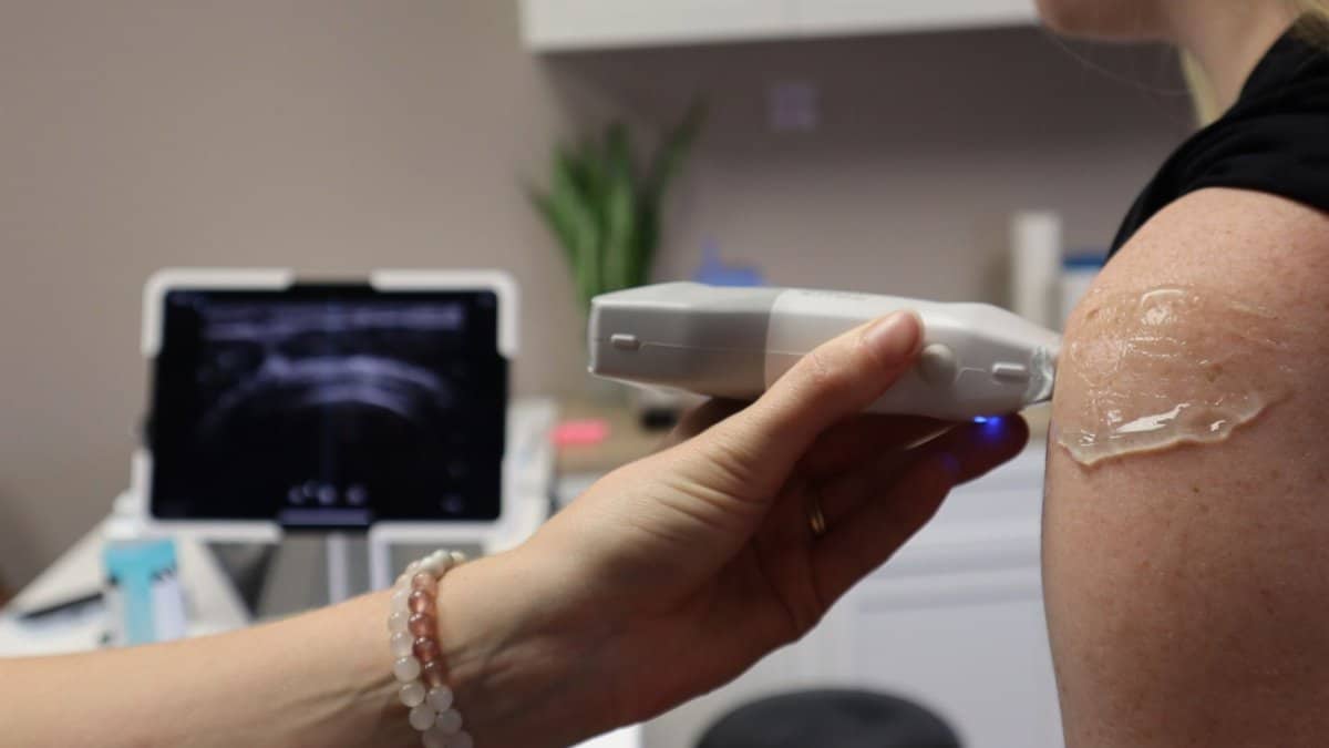 Doctor performing a shoulder ultrasound in a medical office with modern equipment.