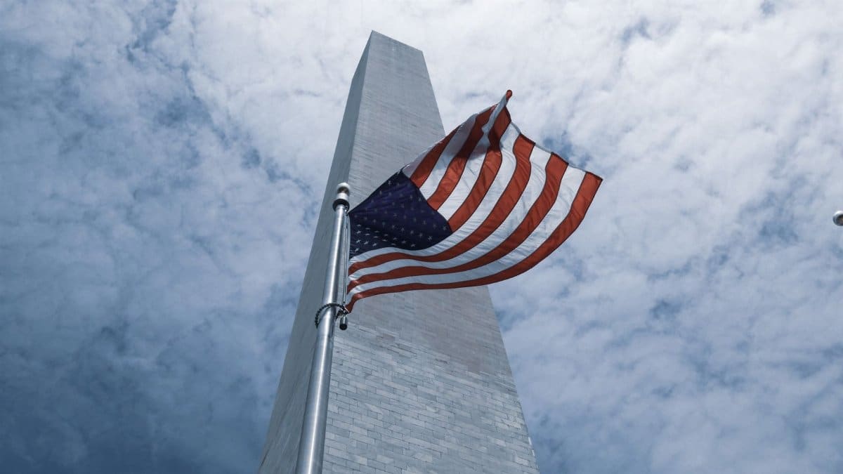 American flag waving in front of the Washington Monument under a cloudy sky in Washington, DC.