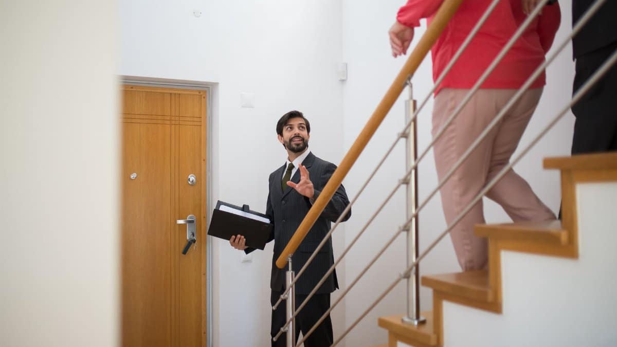 A realtor conducting a house tour with potential buyers on the stairs of a modern home.