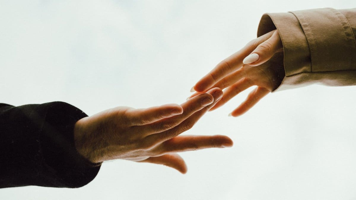 A tender moment captured as two hands reach out towards each other with a soft background.