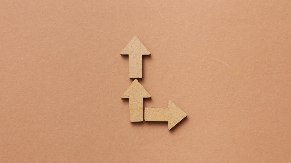 Three cardboard arrows arranged on a brown background, symbolizing direction and choice.