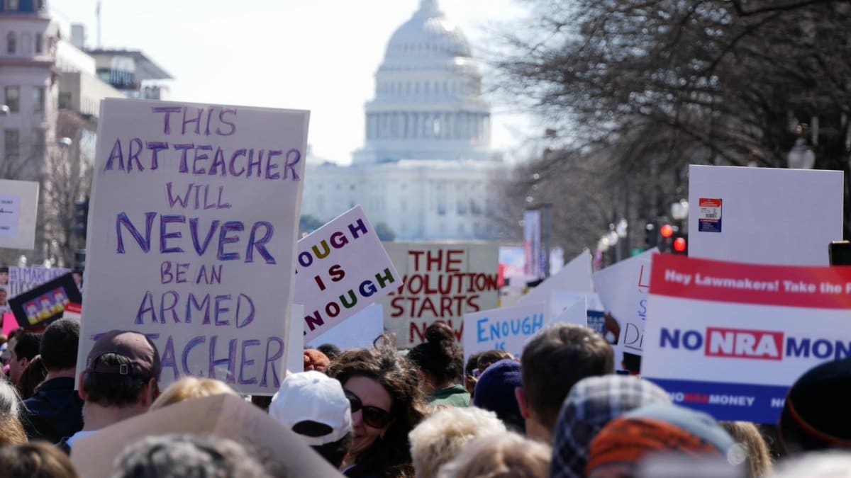 Crowd protesting outside Capitol Building with various banners and slogans.