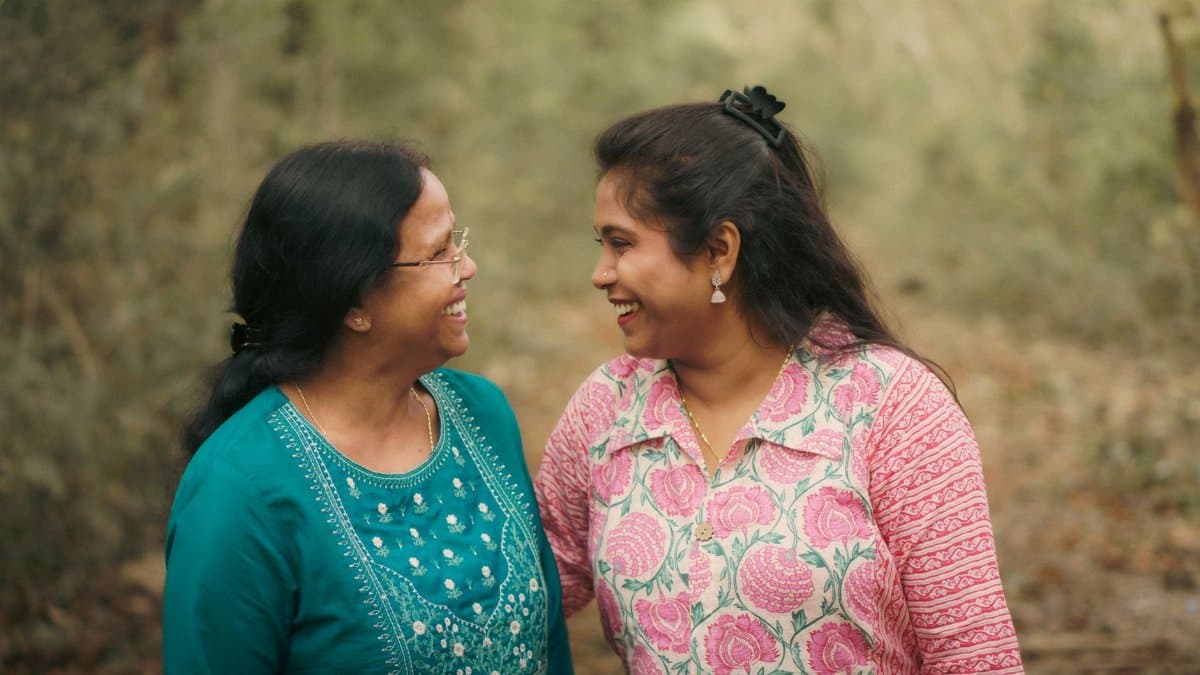 A heartwarming moment between mother and daughter smiling warmly in a forest path.