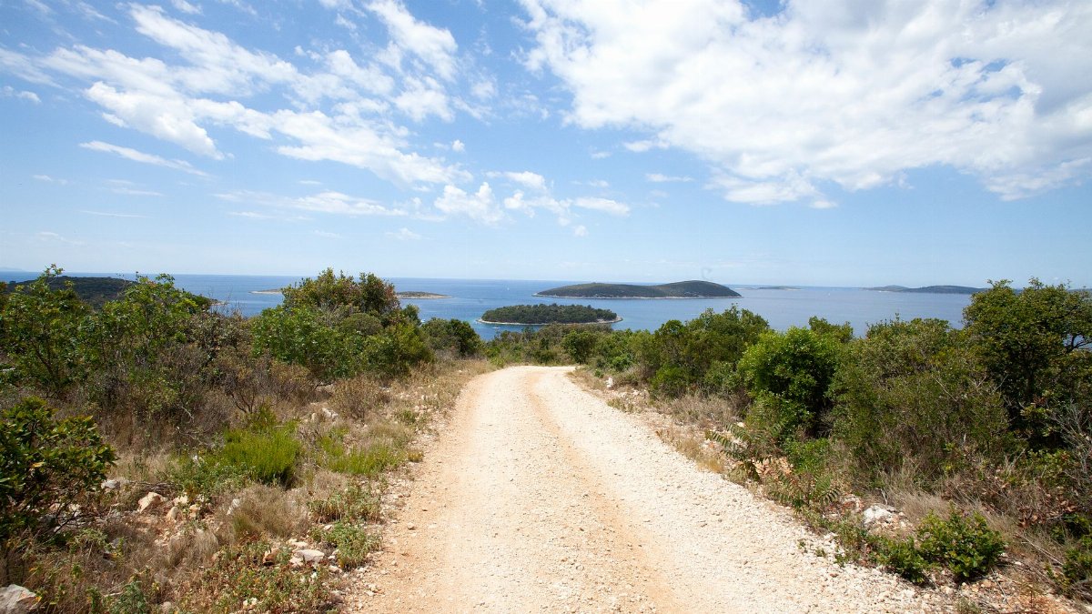 Picturesque dirt road with coastal view in Šolta, Croatia, under a bright summer sky.