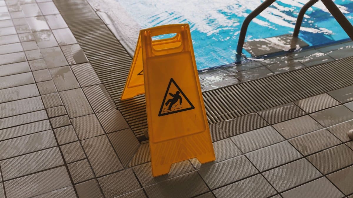 A caution wet floor sign placed near a swimming pool to ensure safety around the slippery area.