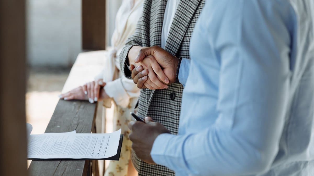 A close-up of hands shaking over a signed property agreement, symbolizing a successful real estate deal.