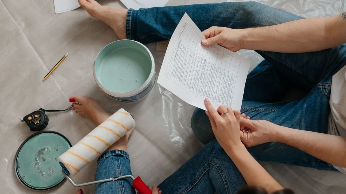 A couple sitting on the floor planning home renovation with paint, documents, and tools.