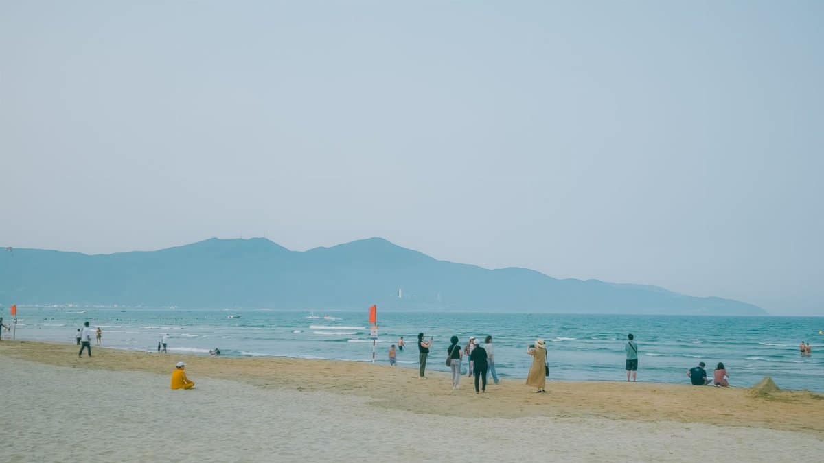 A serene beach in Vietnam with visitors enjoying the coastal scenery and distant mountains.