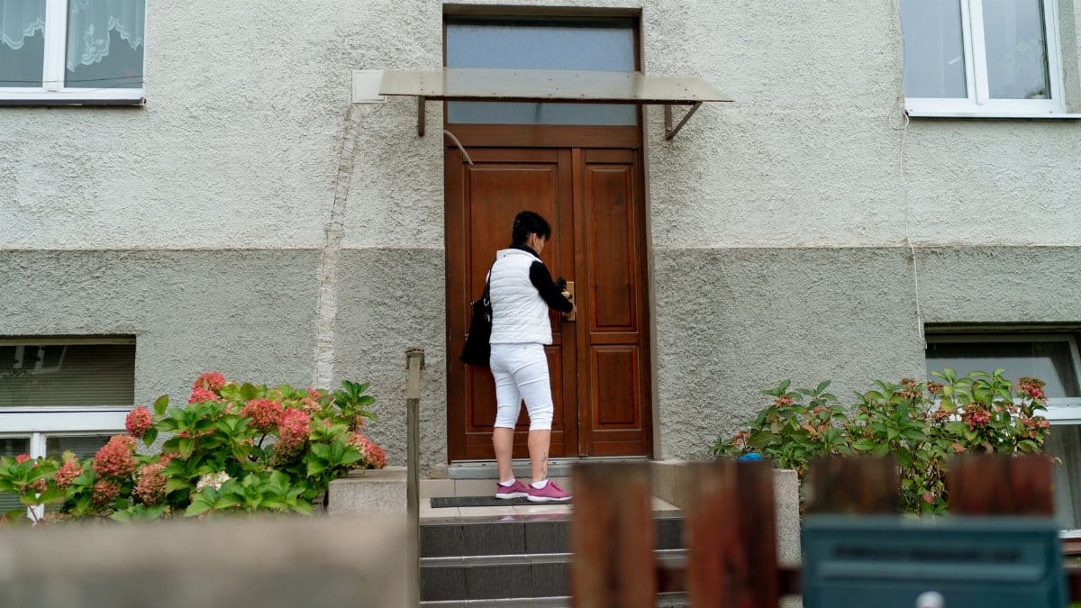 Woman in white outfit unlocking door of a residential building in Prague.
