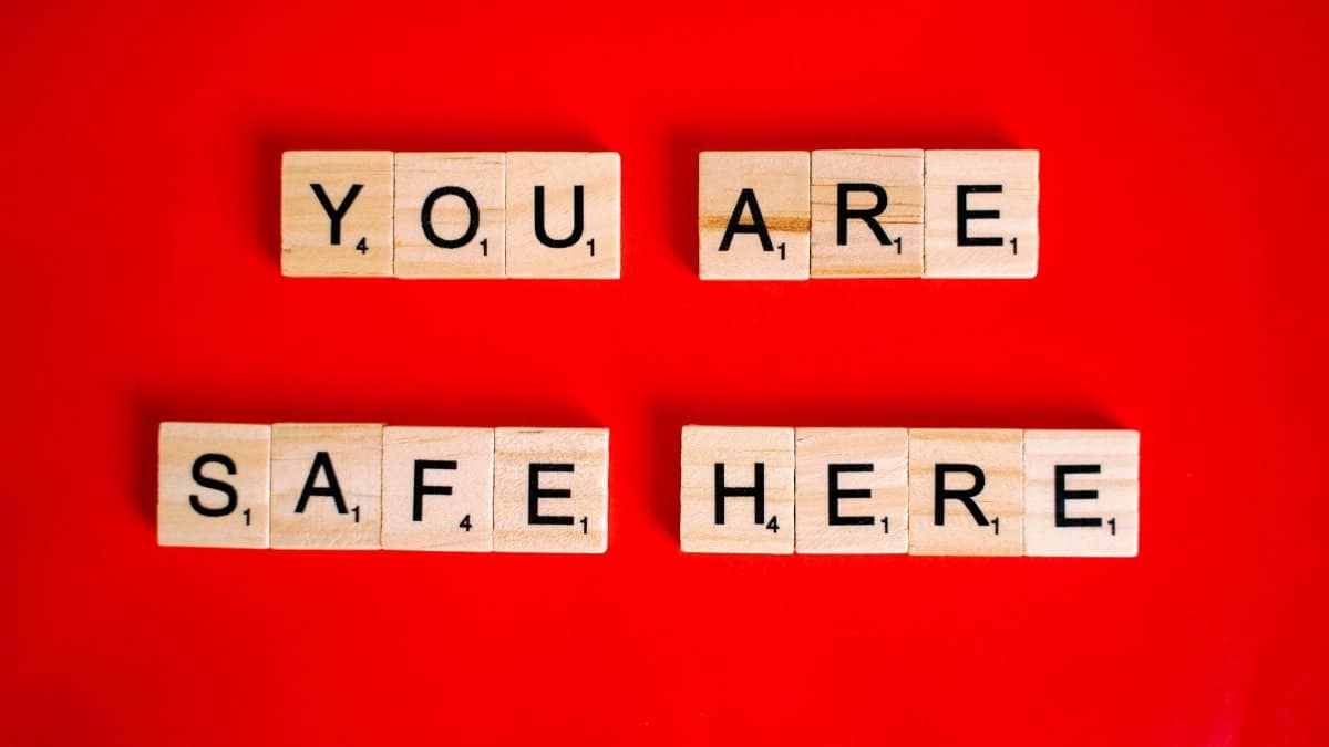 Wooden Scrabble tiles display 'You Are Safe Here' against a red background, symbolizing safety.