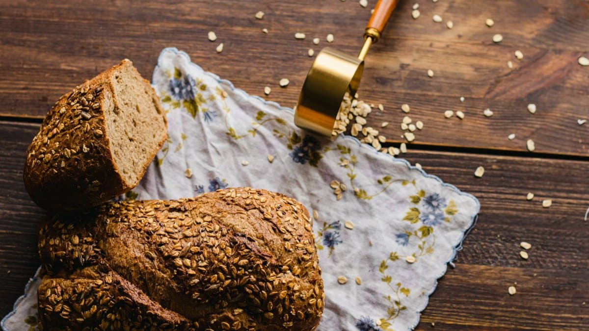 Rustic style whole grain bread loaf with oats on floral cloth and wooden table.