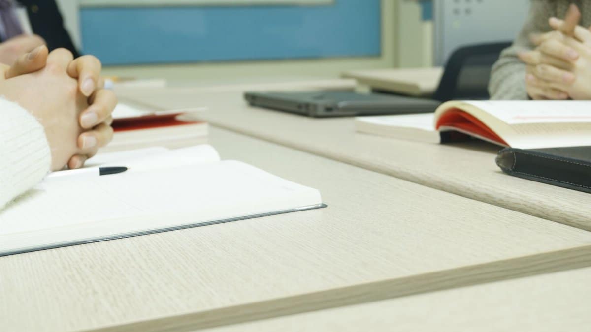 Close-up of a professional meeting setup with hands, laptops, and notebooks on a wooden desk.