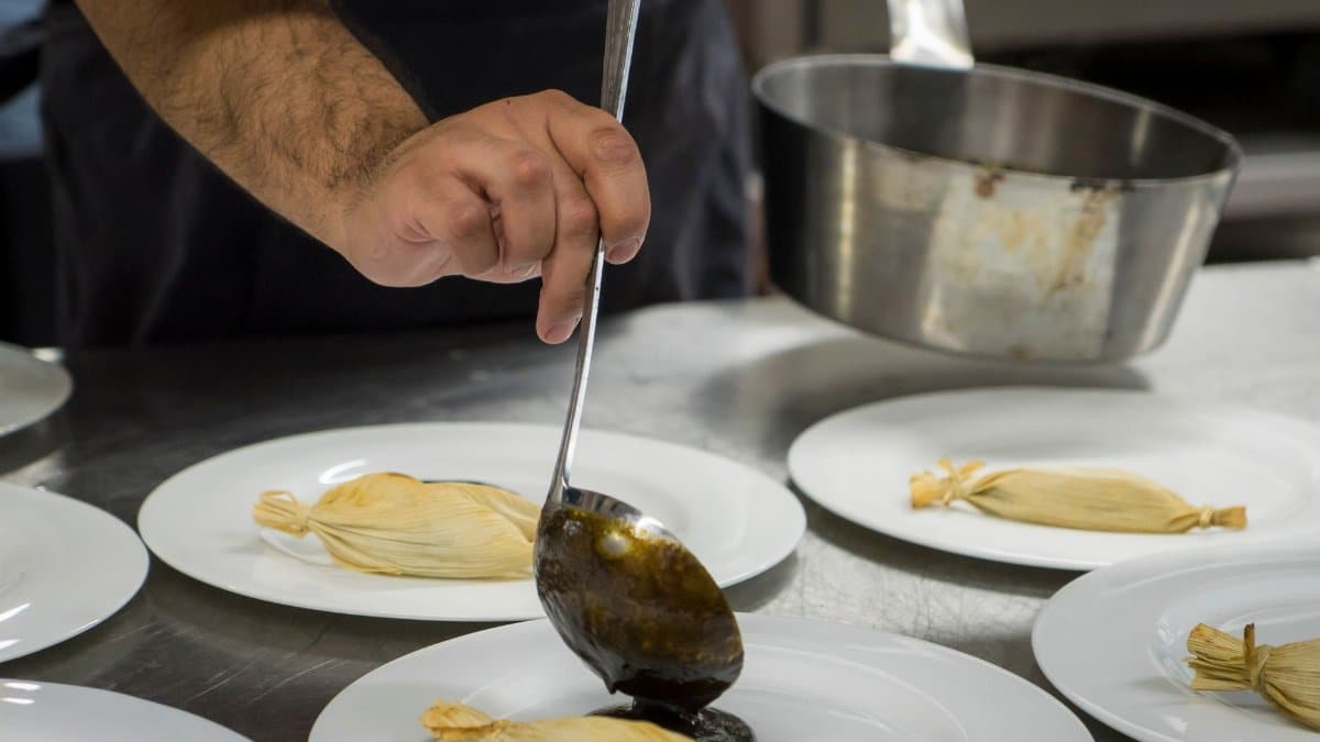 Chef plating gourmet dishes with sauce in a professional kitchen setting, showcasing culinary skills.