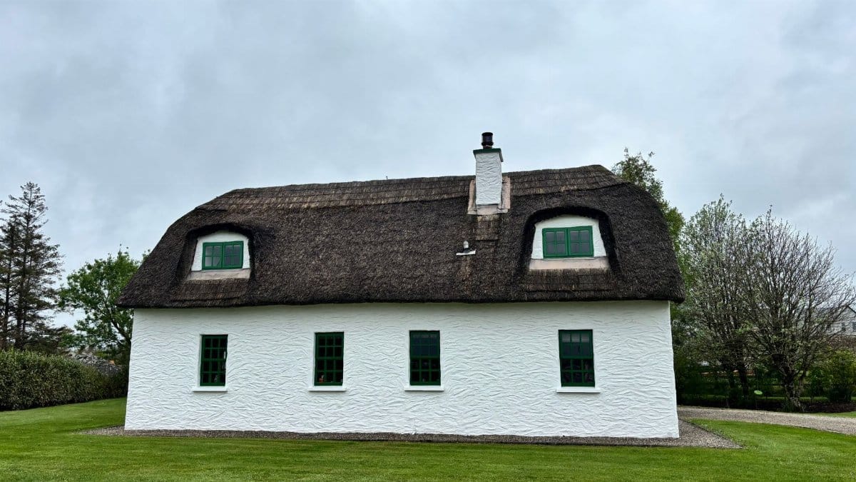 Picturesque thatched roof cottage in Kinvarra, Ireland, set against a lush green landscape.