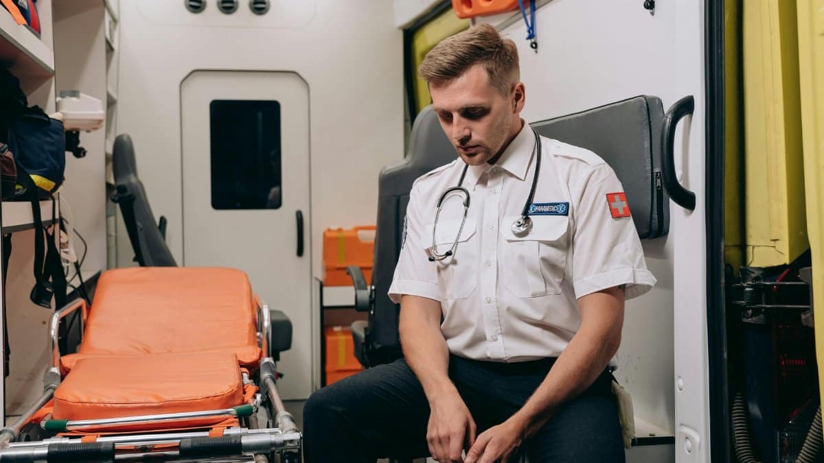 A paramedic takes a moment to rest inside an ambulance, seated with eyes closed.