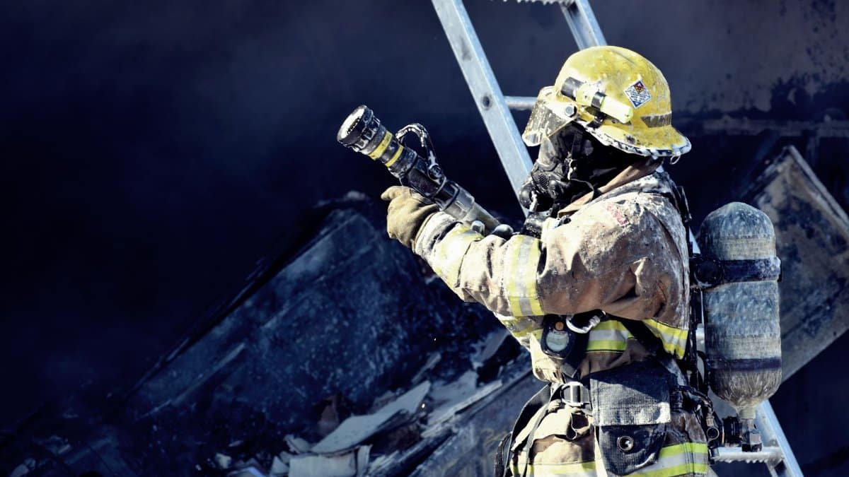 A firefighter in full gear fighting a fire with a hose, emphasizing courage and safety.