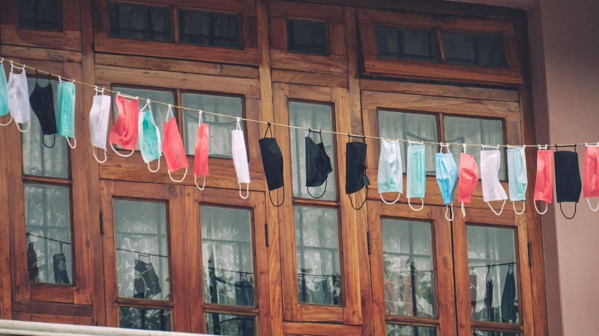 Colorful face masks hanging on a clothesline in front of a wooden window, representing safety and protection.